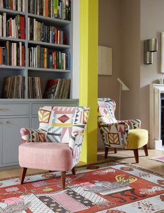 Living room with bright yellow painted architrave, open shelving and pink chair