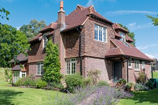 exterior of a 1930s redbrick farmhouse with lavender lined path and lawns with blue skies