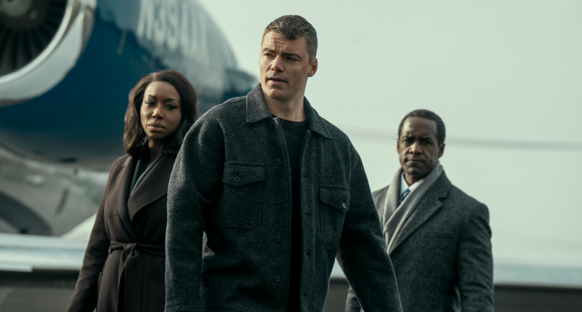 gabriel basso as peter sutherland, amanda warren as catherine weaver, and albert jones as aiden mosley exiting a plane on a jetway in a still from the night agent season 3