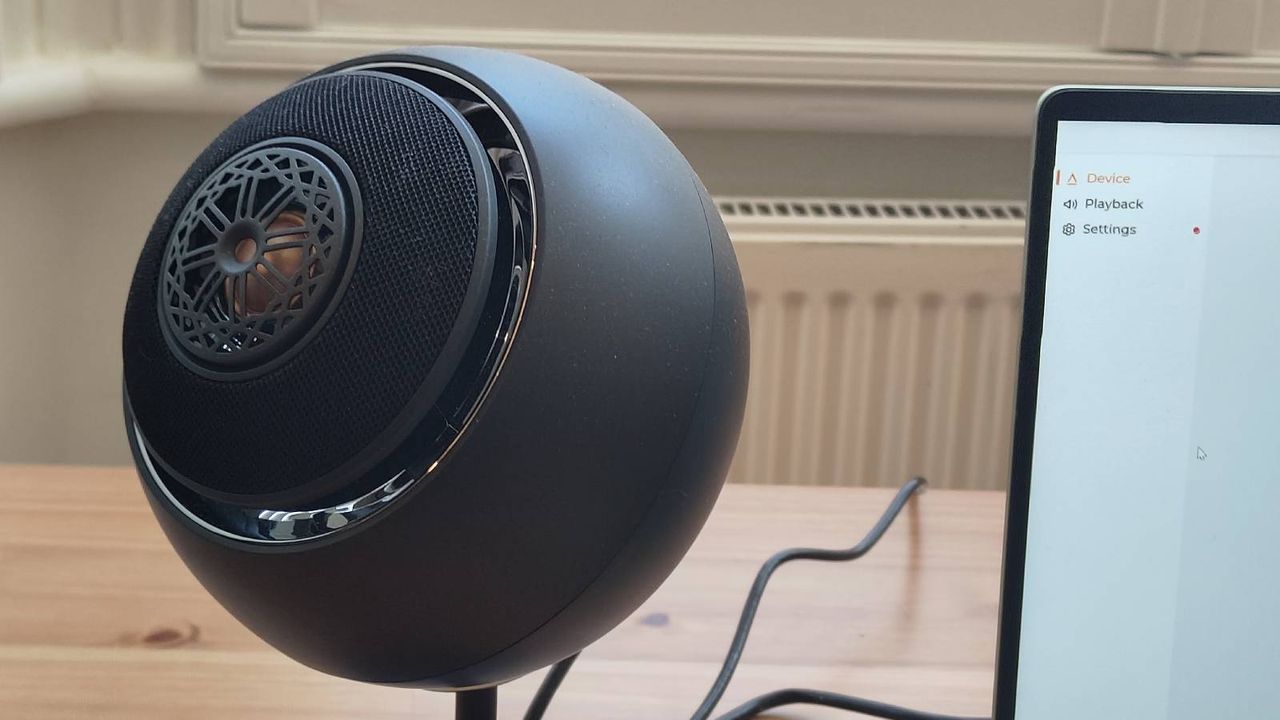 The Creative Pebble Nova on a brown table, connected to a green laptop.