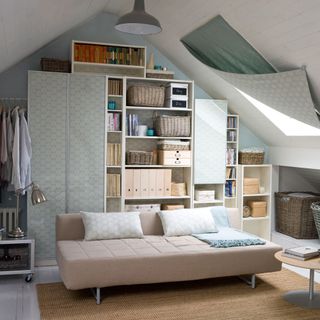 white and blue room with a beige sofa with light blue cushions on top of a woven carpet and a white open cabinet filled with books and accessories