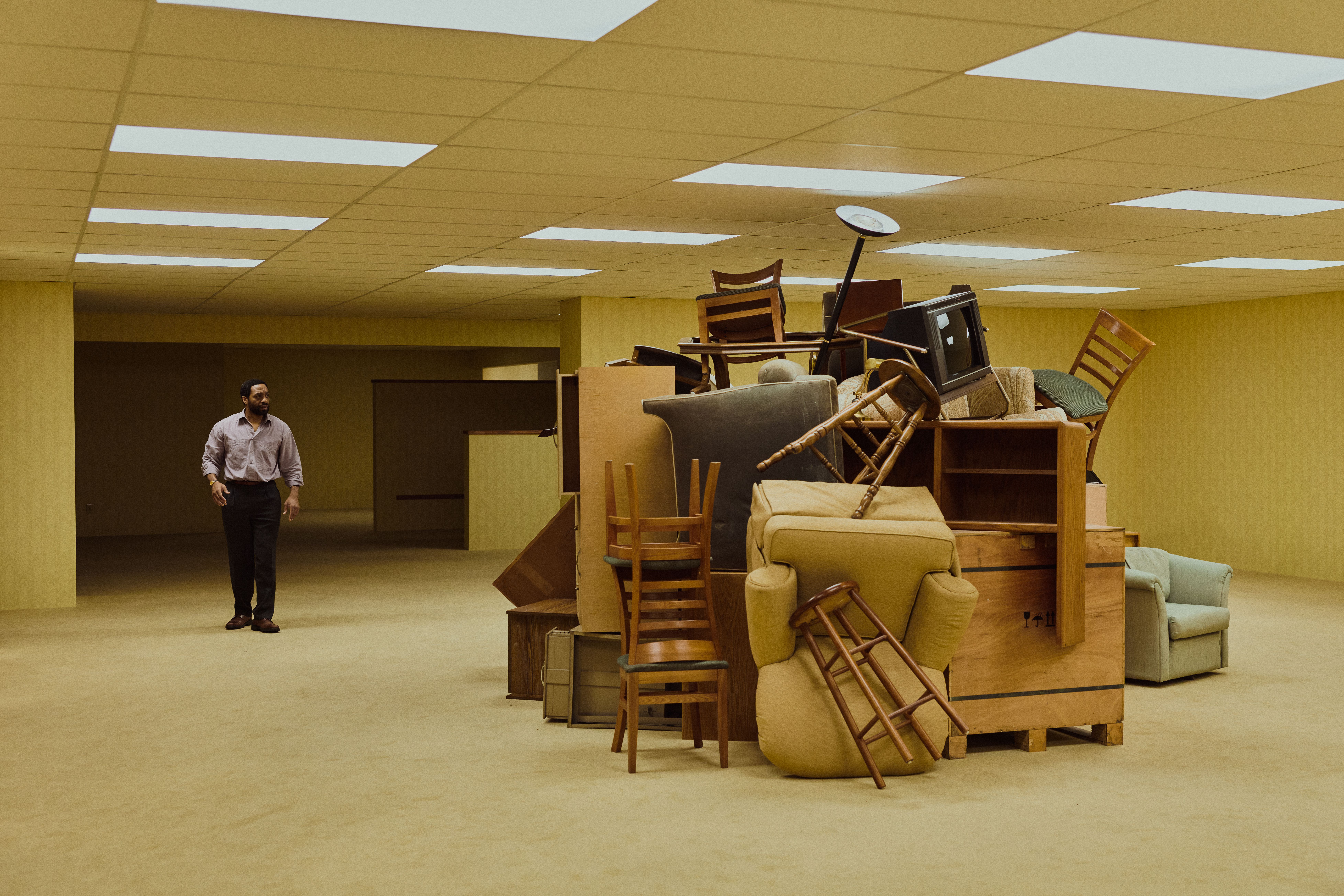 A pale yellow film set with textural wallpaper, minimal decor, and people wandering through it.
