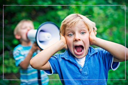 Little boy with hands over his ears with child holding megaphone behind him