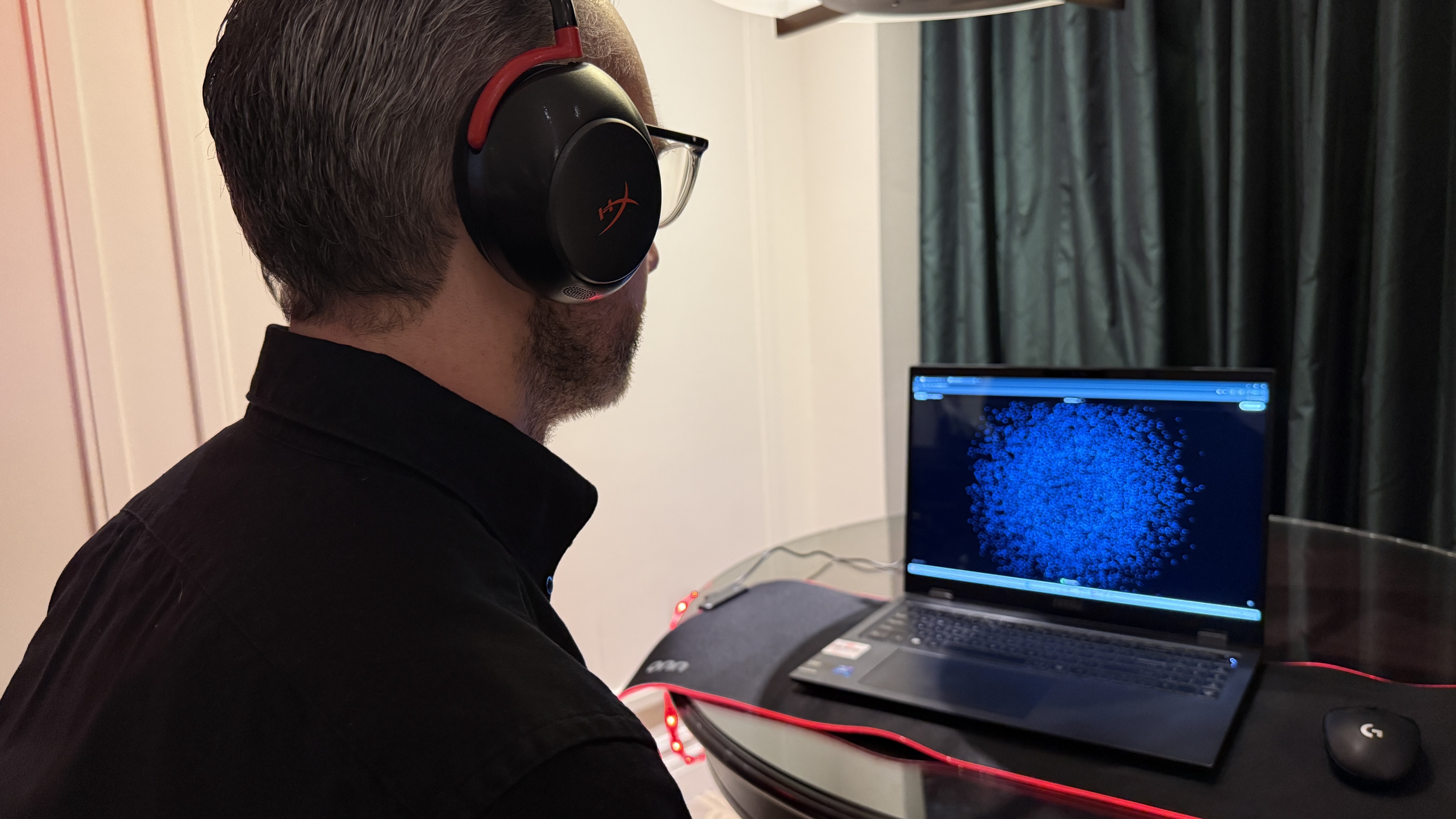 The HyperX Neurable prototype worn by a man, who is looking at a laptop with a cloud of dots on it