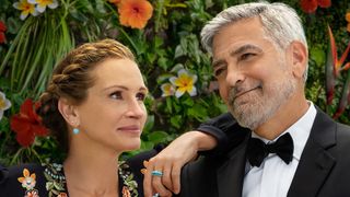 (L to R) Julia Roberts and George Clooney in front of flowers in the poster for Ticket to Paradise.