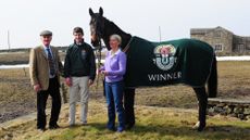 Auroras Encore at home after his National win, wearing his winner's rug with his trainers and jockey