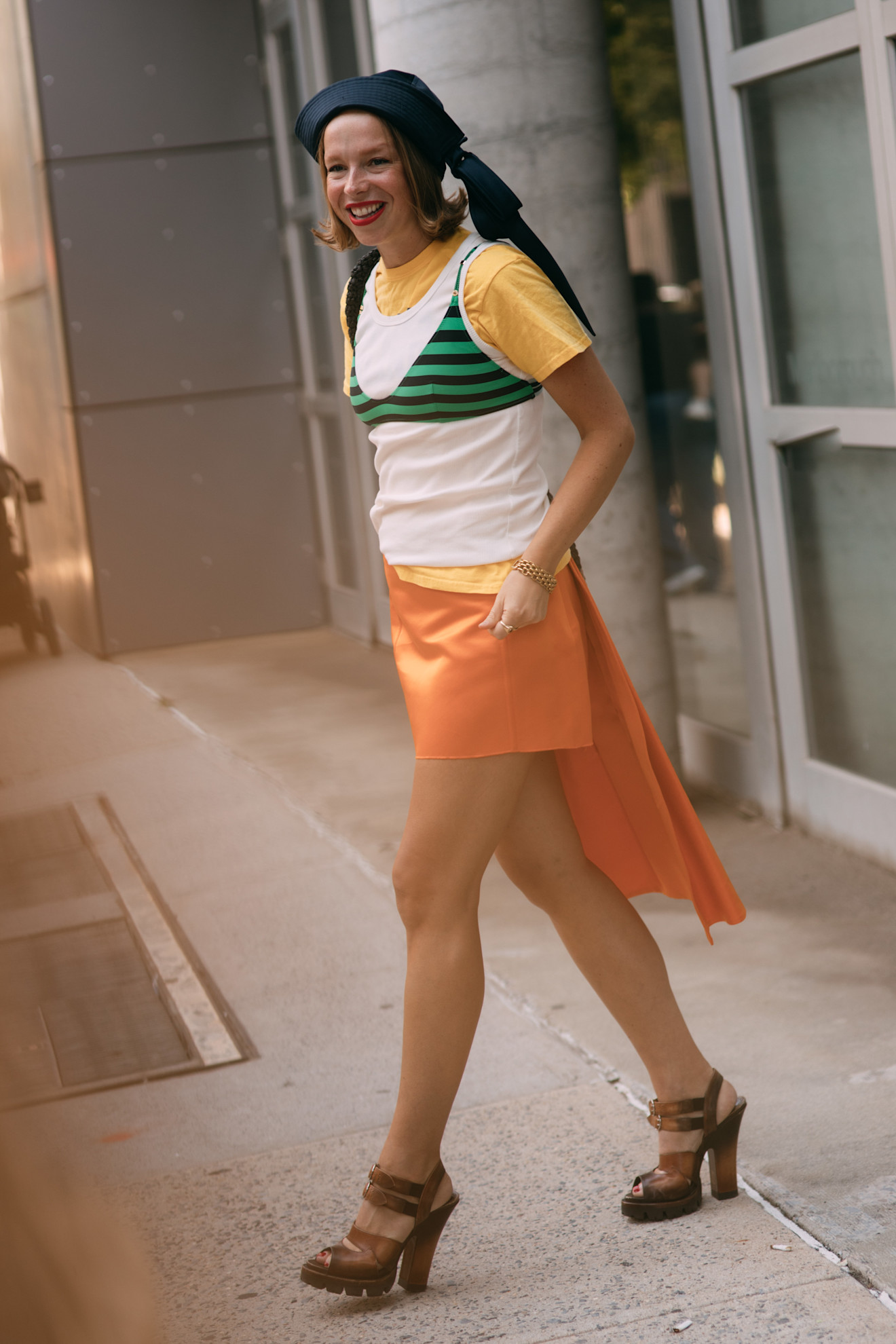 fashion week attendee wears layered t-shirts, orange skirt, brown heels