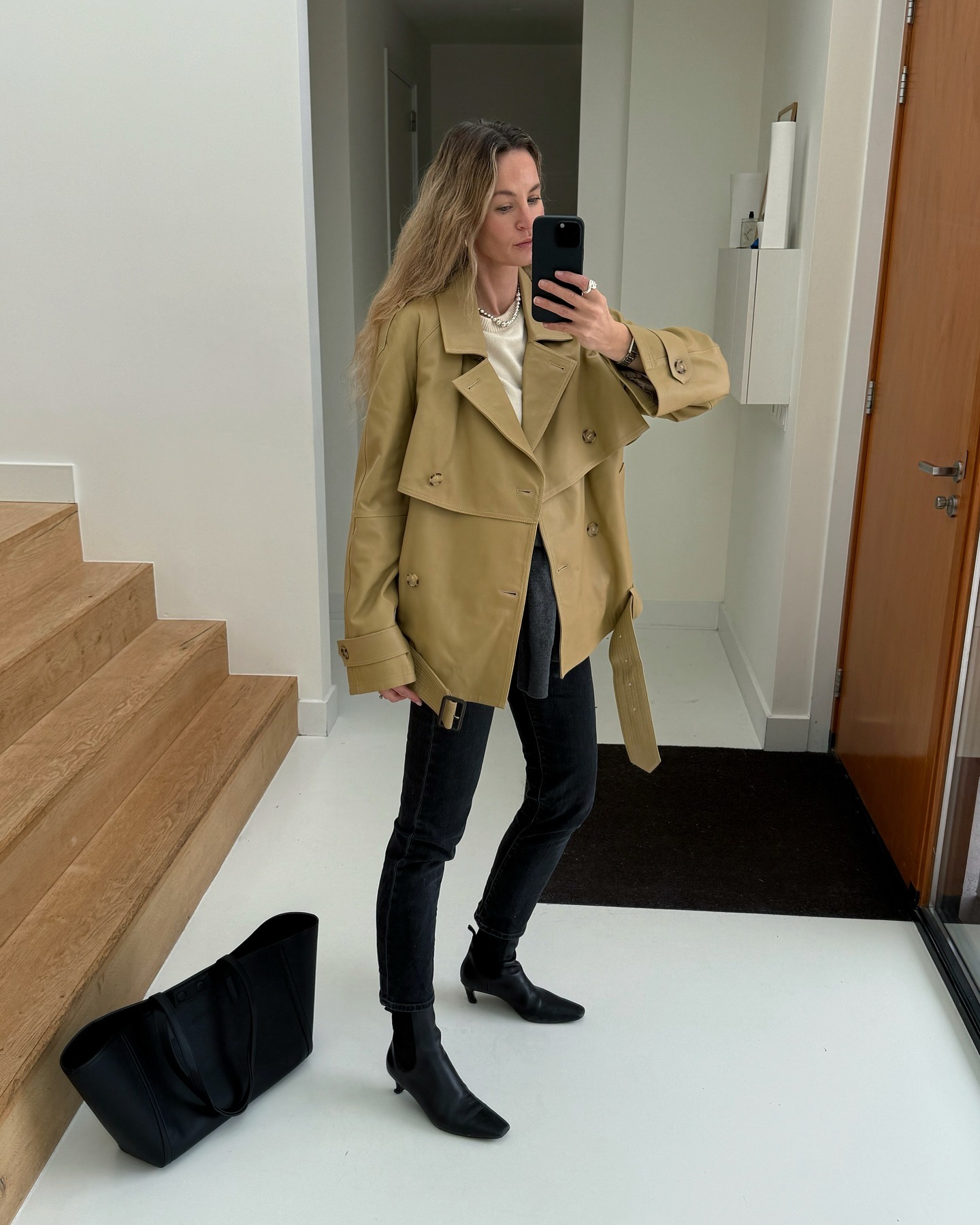 Influencer Anouk Yve wearing a tan trench coat, black skinny jeans, and black ankle boots