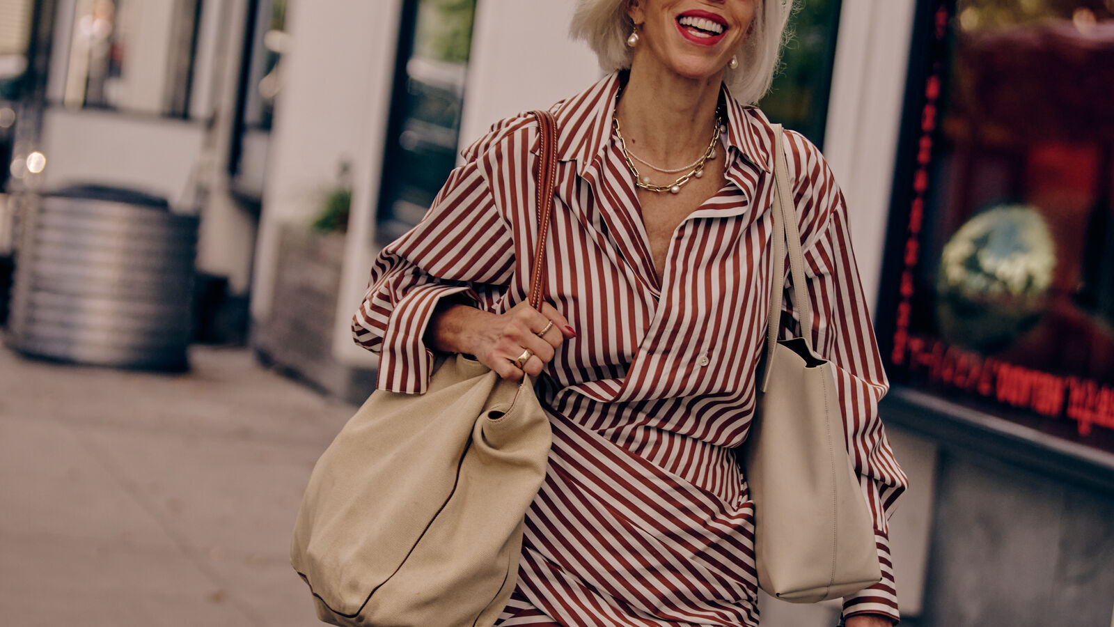 a woman smiling in a striped red dress carrying two white tote bags