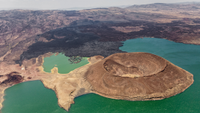 Aerial view of the Nabuyatom Volcano at the edge of Lake Turkana in northern Kenya showing its almost uneroded caldera, more than a kilometer wide. Black lava covers the land to the horizon.