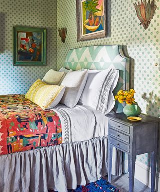 colorful bedroom with green patterned wallpaper, green patterned headboard, colorful throw, colorful artwork, red and blue rug and gray bedside cabinet