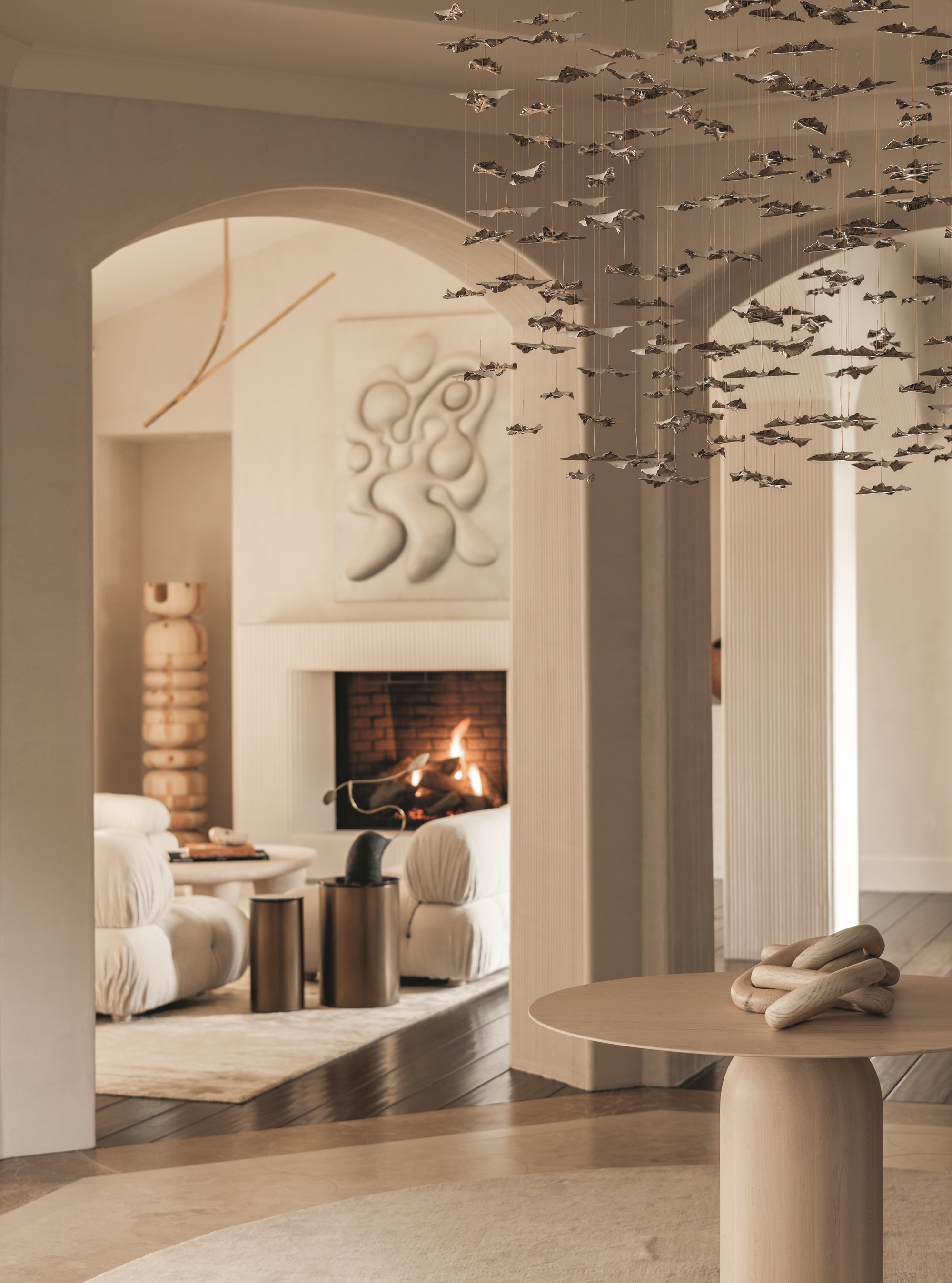 modern entryway with arched doorways, round table with sculptural hanging overhead, with modern beige living room in the background