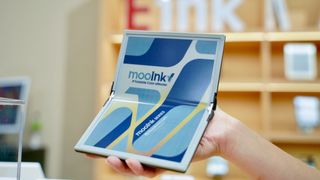A hand holding up the Readmoo mooInk V folding ereader in front of a book shelf