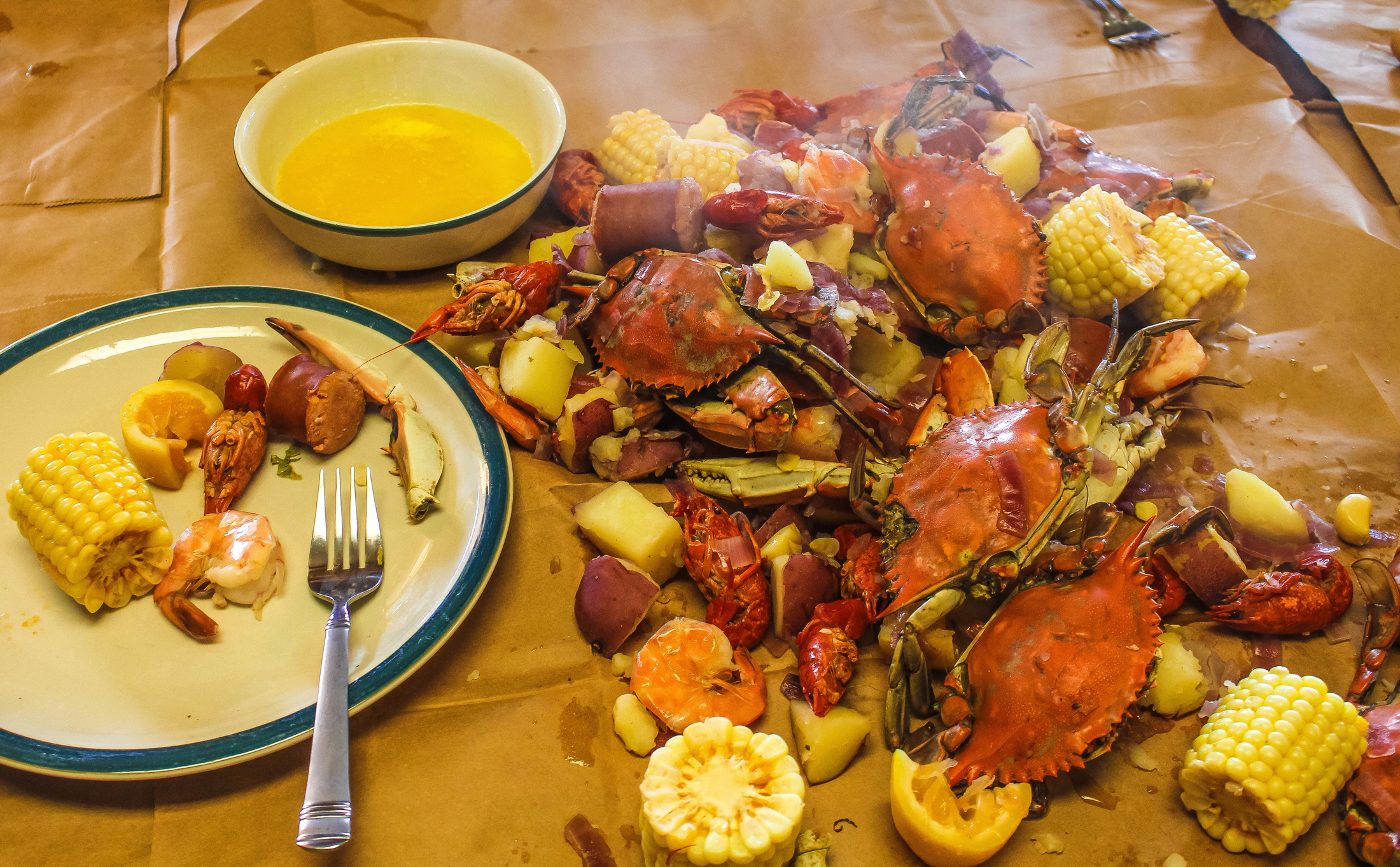 Traditional Cajun seafood boil served on brown paper with a bowl of melted butter including corn potatoes onions lemon carb crawfish shrimp andouille sausage in a spicy boil