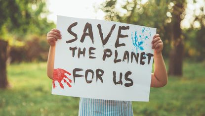A placard reading ‘Save the planet for us’ being held up by a child