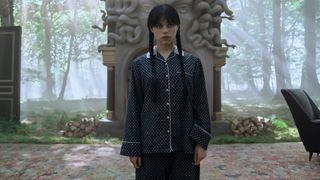 Wednesday Addams standing in a courtyard surrounded by a forest in Wednesday season 2 part 2