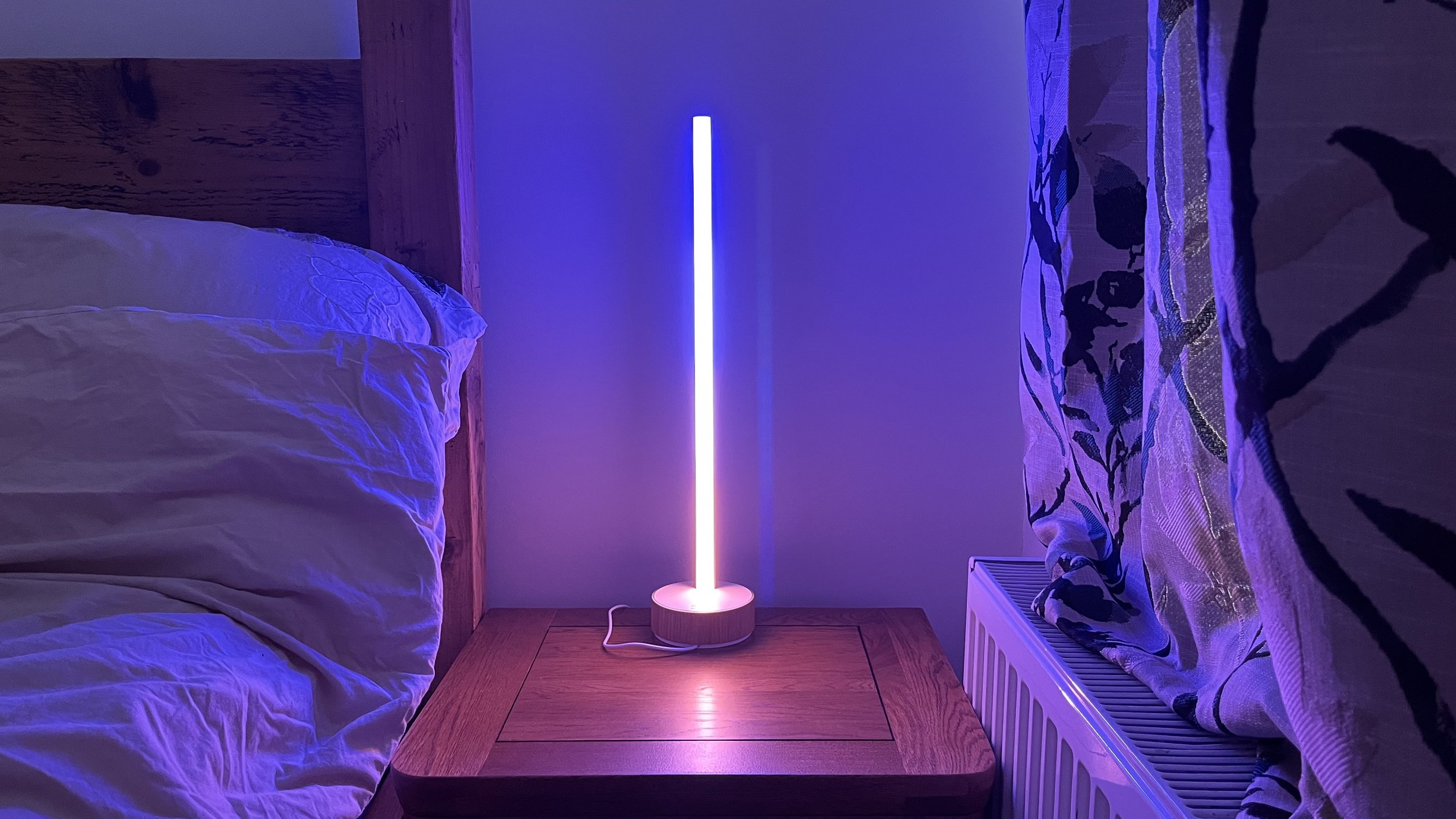 A Philips Hue Signe lamp sitting on a beside table next to some curtains