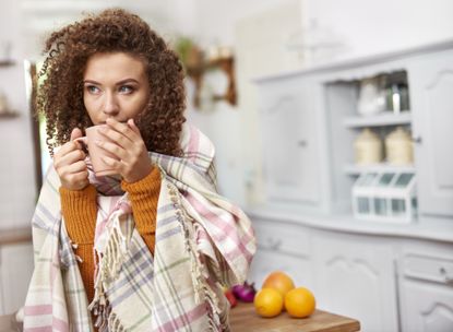 Vitamin D foods: Young woman wrapped in blanket drinking hot tea