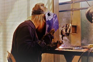 A student in a facemask welds a piece of machinery