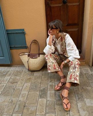 Julie Sergent Ferreri in a floral set, leather sandals, and a straw tote bag.