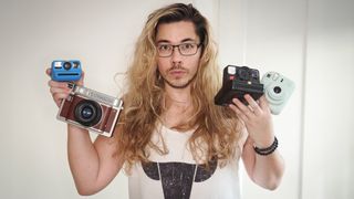 Reviewer James Artaius holding a selection of Polaroid, Instax and Lomography instant cameras