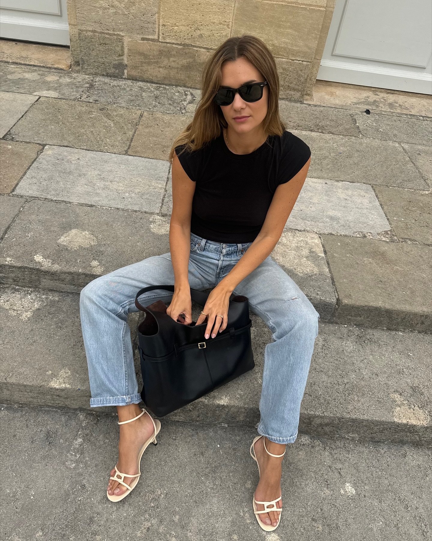 An image of @annelauremais wearing stovepipe jeans with sandals and a black t-shirt.