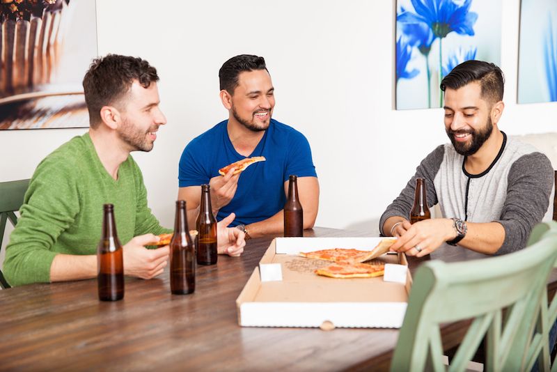 Three guys hang out together, eating pizza