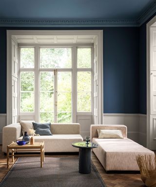 Blue living room with painted blue walls and ceiling, cream chunky sofa, large white window, wooden parquet flooring, gray rug, black side table, wooden side table
