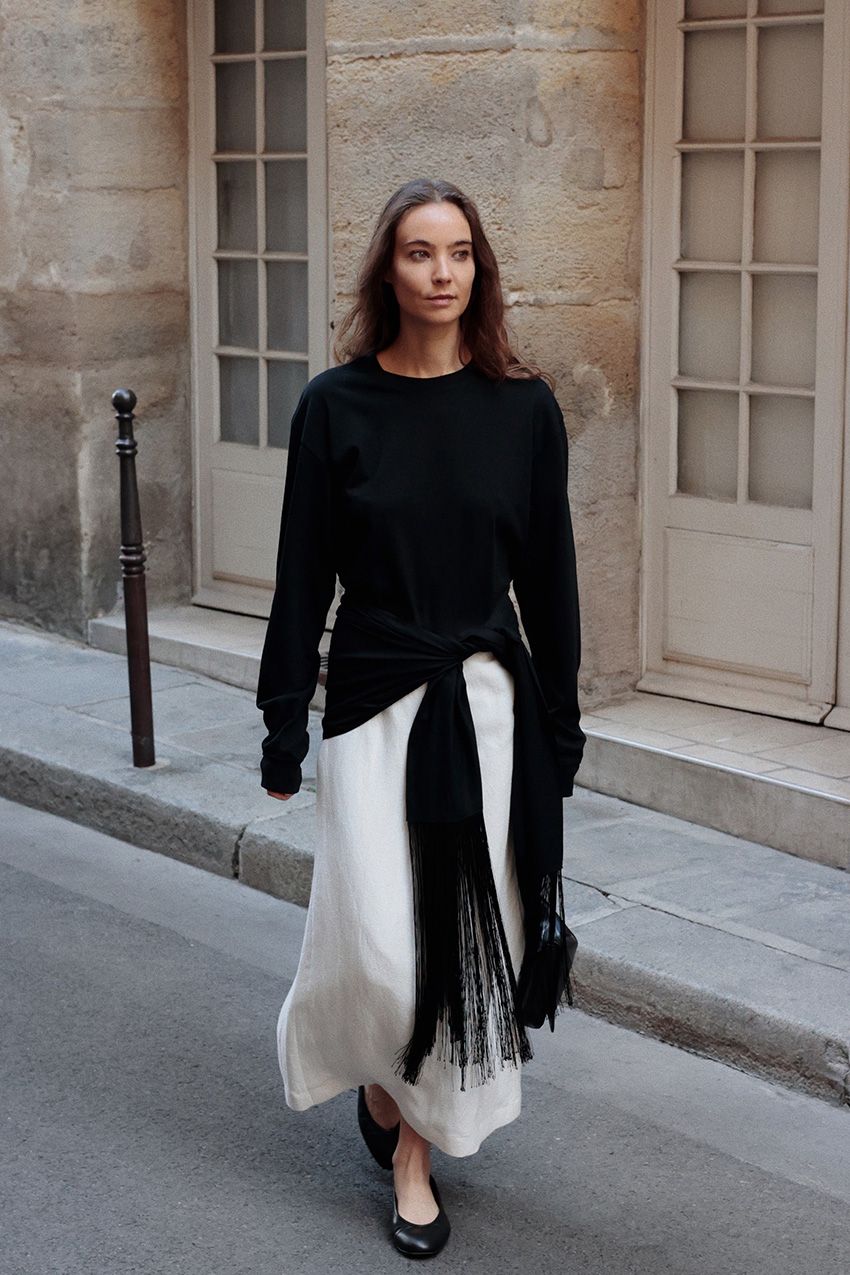 Fall shoe trends in Paris are shown in a photo of a woman crossing the street wearing the high-vamp trend styled with a black sweater and white skirt