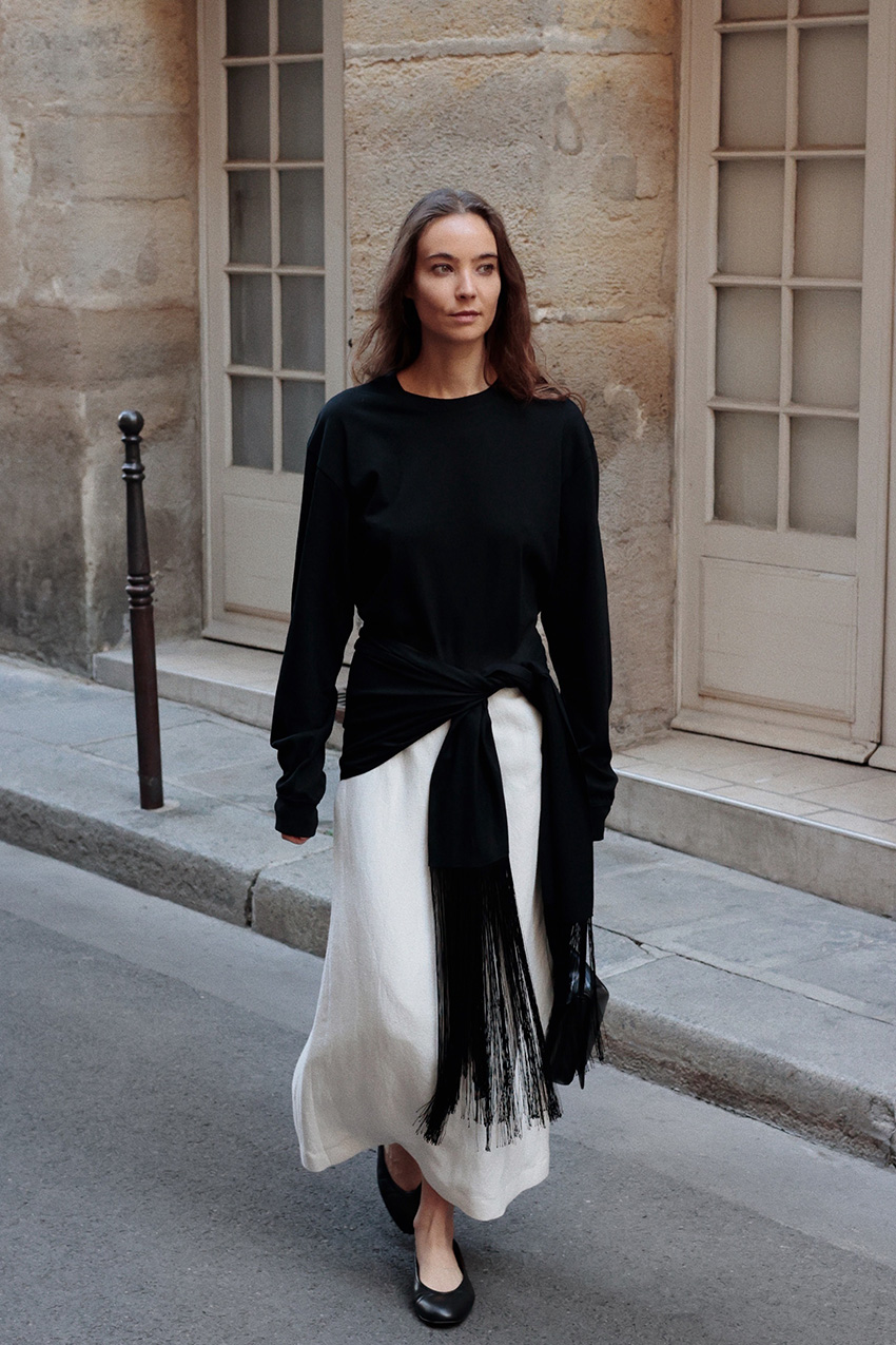 Fall shoe trends in Paris are shown in a photo of a woman crossing the street wearing the high-vamp trend styled with a black sweater and white skirt