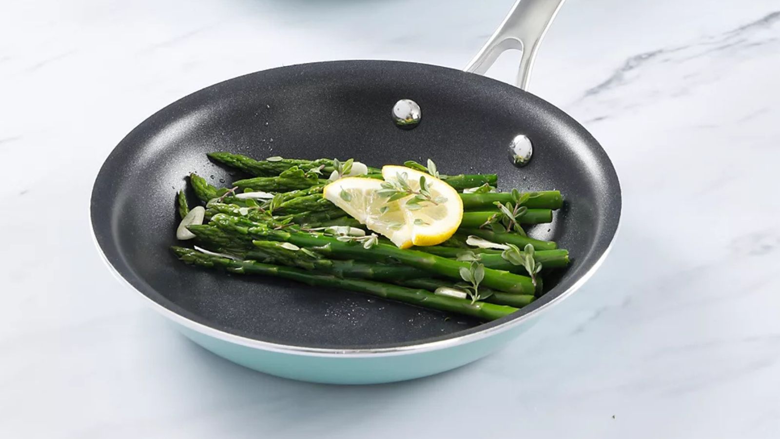Pale blue frying pan with blue enamel exterior, with a handful of asparagus and a slice of lemon inside