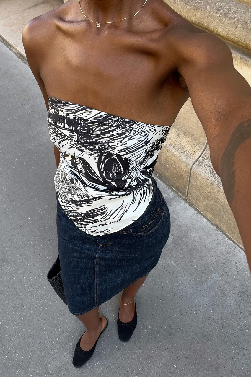 A woman wearing a tube top, denim skirt, and black pointed toe shoes.