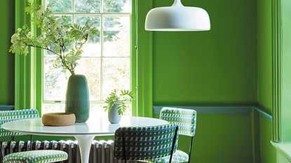 Bold green dining room with white pedestal dining table and pendant light