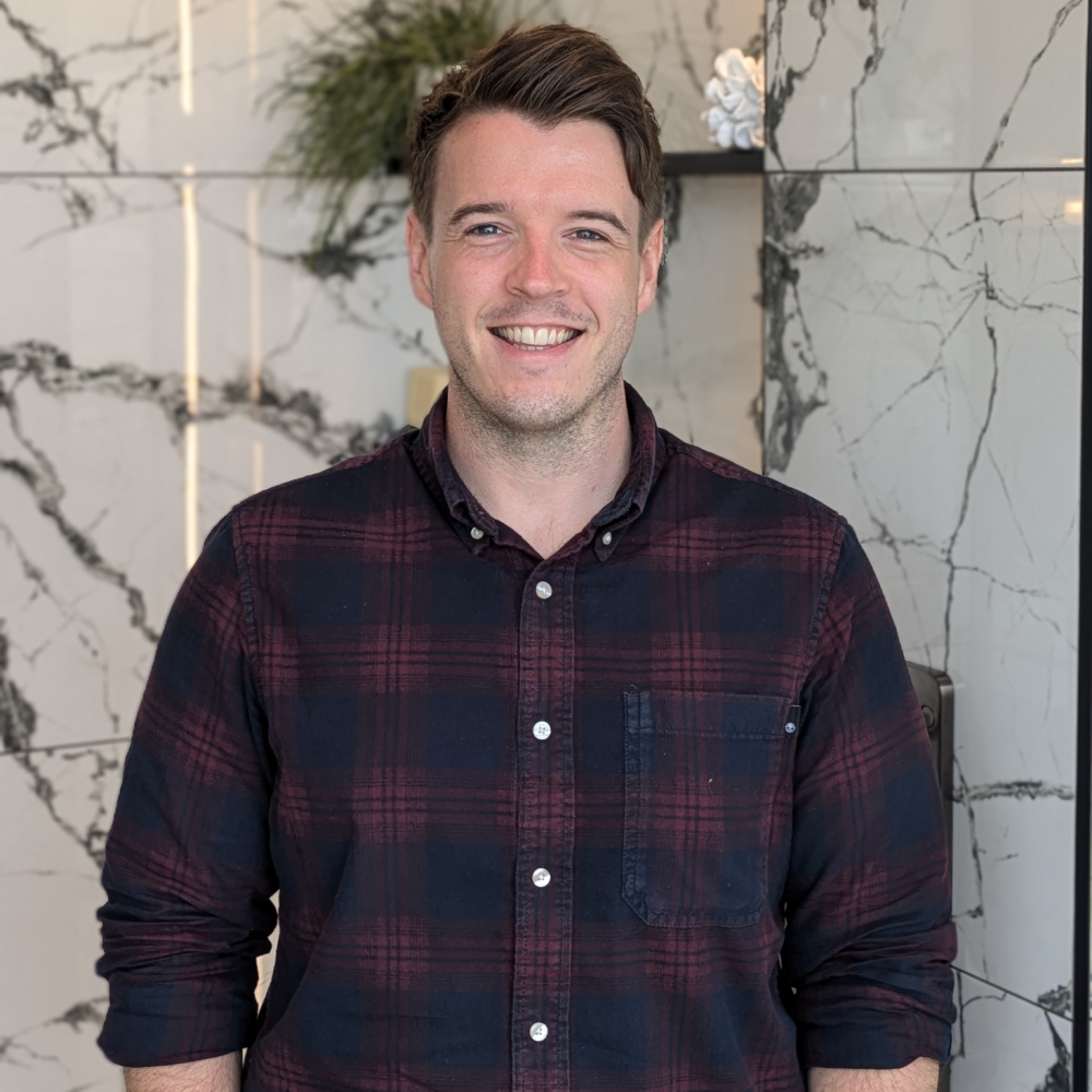 male with short brown hair wearing plaid shirt stood in bathroom