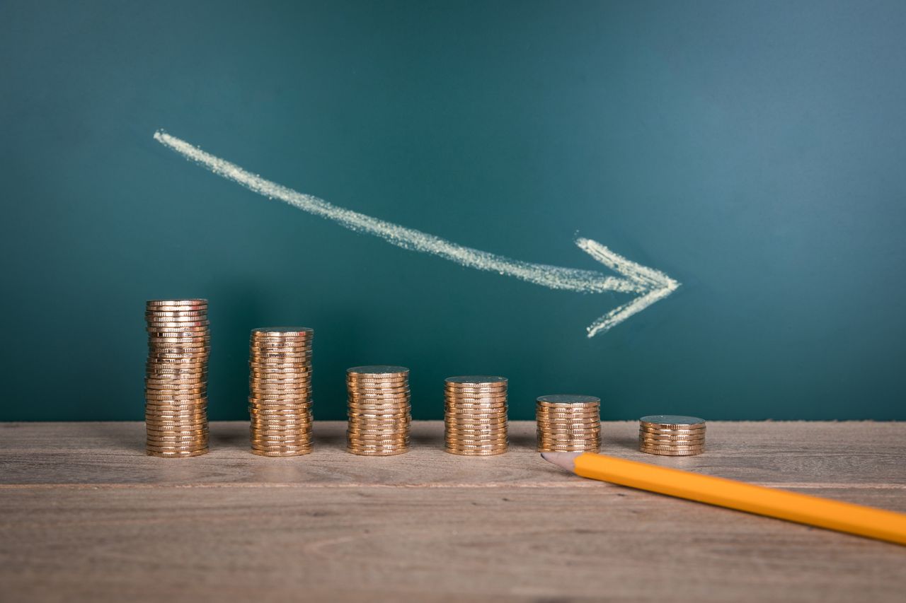 image of descending stacks of coins with a downward arrow above them