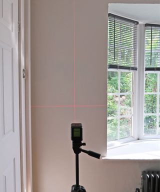Laser level beam on wall with window casement and black blinds in background