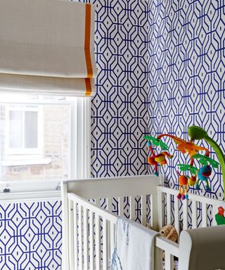 Gender neutral nursery room ideas with patterned blue and white geometric print wallpaper and a white cot.