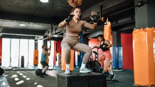 Woman doing functional training by jumping on box at gym