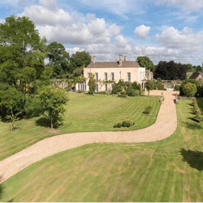 country house sits at the end of gravel path flanked by green grass and trees