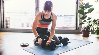 Kneeling woman adds weight plate to adjustable dumbbell