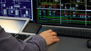 IT technician operating a SCADA industrial control system at a computer station.