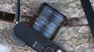 Close-up of the lens on a Leica Q3 43 camera sat on a wooden slatted bench