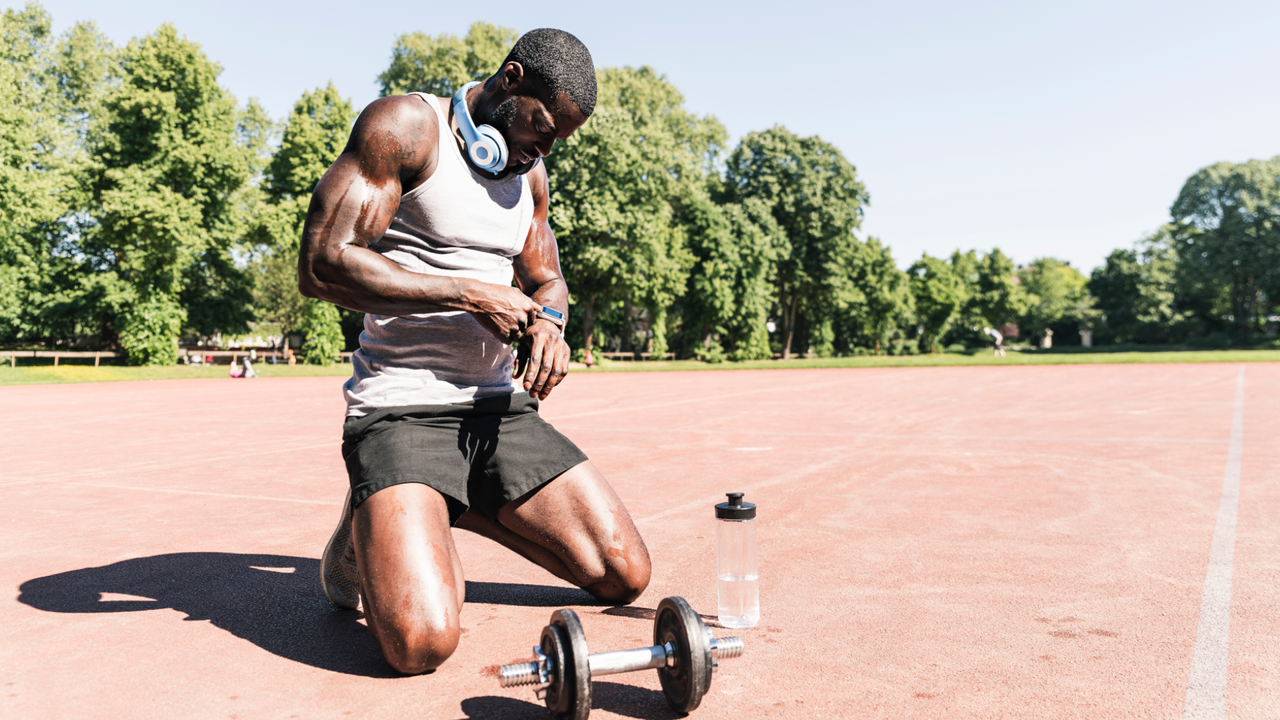 Man on his knees looking at his watch with a dumbbell in front of him