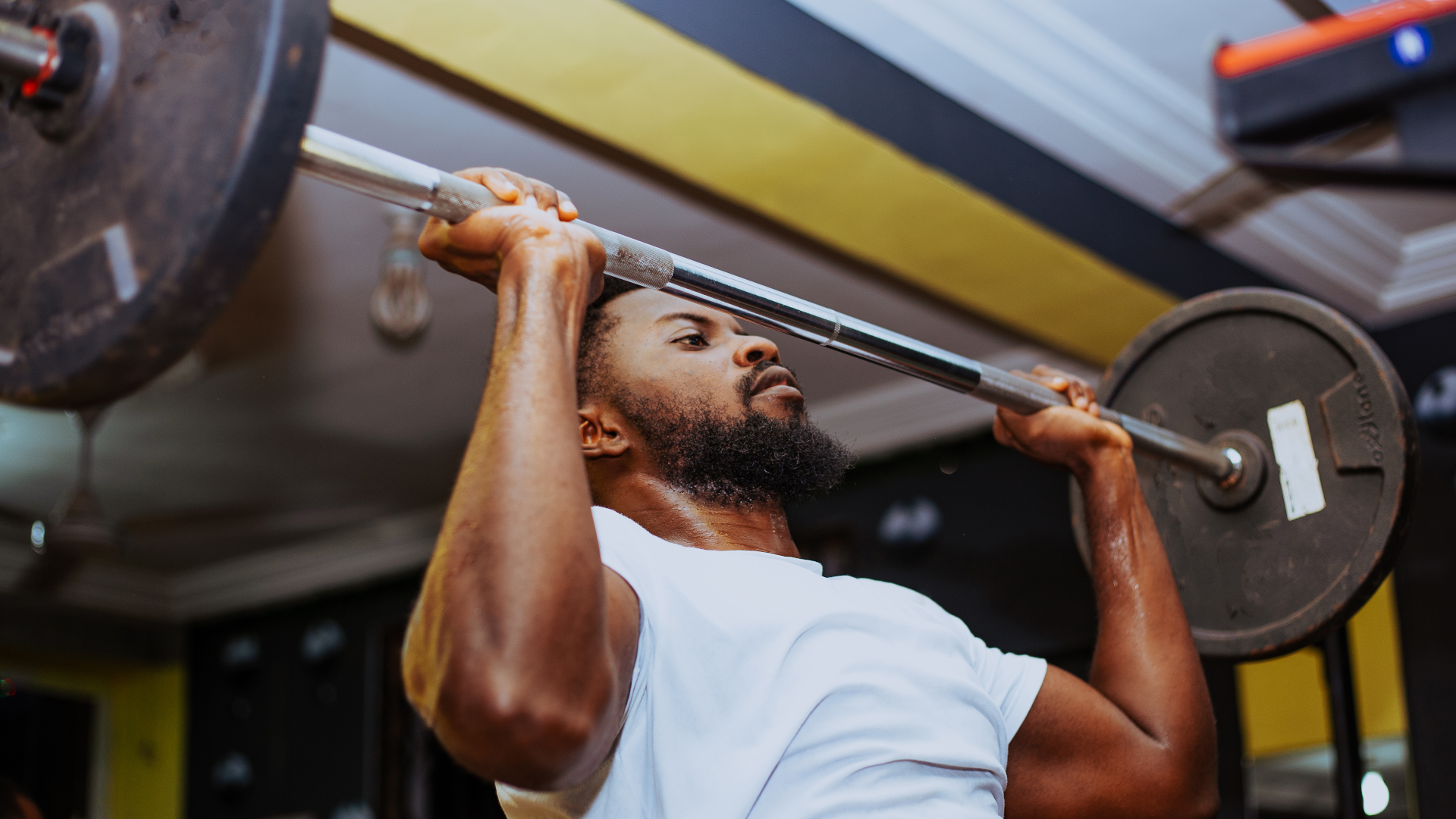 A man performing a barbell overhead press at the gym