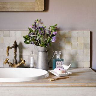 Tiled splashback in a bathroom with a toothbrush and a vase of flowers