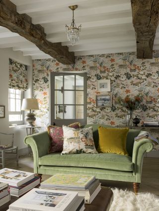 Traditional living room with exposed beams, floral wallpaper, green couch and classic soft furnishings