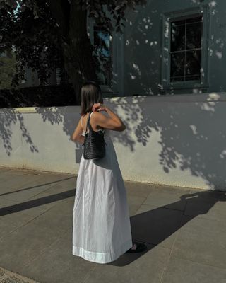 Woman on street wears white dress and woven bag