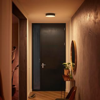 a hallway with a black front door, a large round mirror and a ceiling light above
