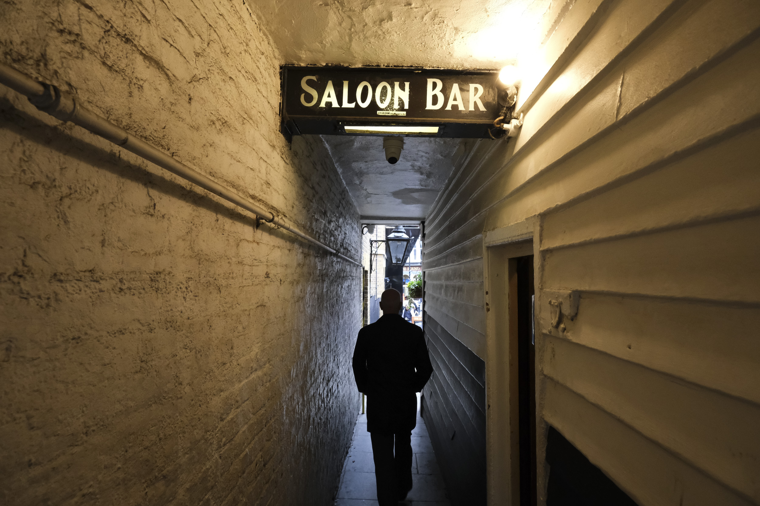 Dark alleyway with a lone silhouette and bar sign above, taken with the Fujifilm X-M5