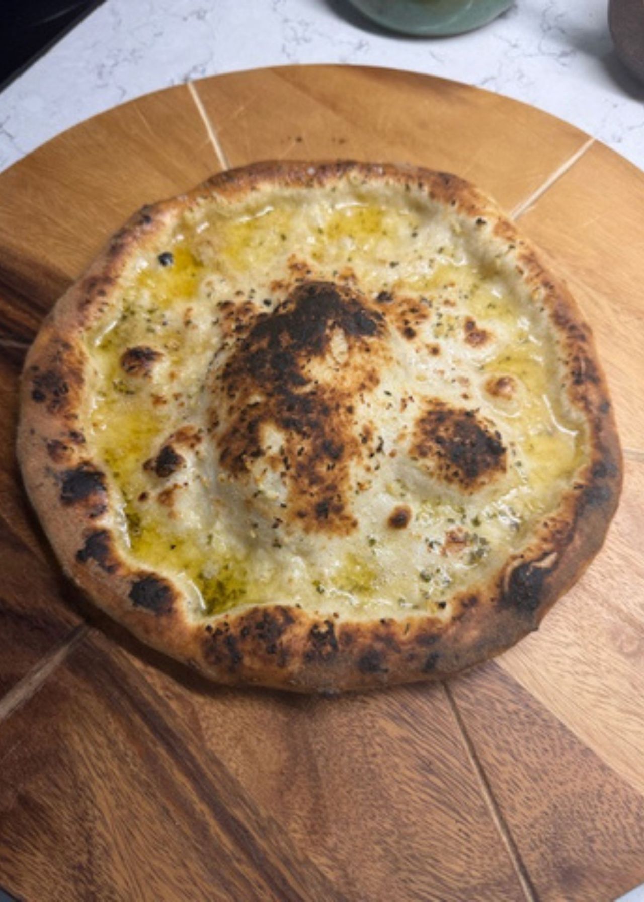 Uncut garlic pizza bread on a round wooden chopping board with slice grooves on a kitchen countertop